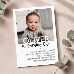 May include: A rectangular birthday invitation card featuring a photograph of a baby. The text reads OLIVER is turning One! followed by event details including Saturday, October 12th at 2pm at The Flower Garden, 123 Main Street, Los Angeles, CA.