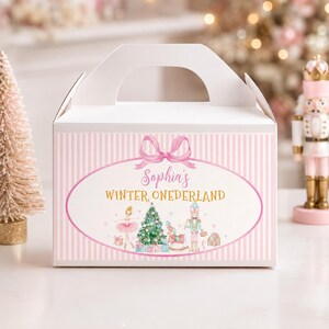 May include: A white gable box with a light pink vertical striped pattern. The front features a pink oval frame with a bow, containing the text Sophia's WINTER ONEDERLAND, a ballerina, a Christmas tree, a rocking horse, and a nutcracker figure.