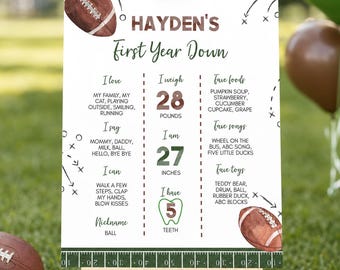 May include: A white milestone birthday sign titled Hayden's First Year Down with football graphics, text listing personal facts, weights in pounds, and height in inches. The board features brown and green text, a football field border, and a tooth icon.