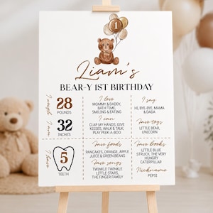 Puede incluir: Un cartel de cumplea&ntilde;os blanco con un oso de peluche marr&oacute;n que sostiene globos con el n&uacute;mero uno. El texto dice Liam's BEAR-Y 1ST BIRTHDAY, enumerando estad&iacute;sticas como 28 pounds, 32 inches, 5 dientes, comidas, canciones, libros y juguetes favoritos.