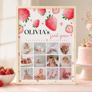 K&ouml;nnte beinhalten: Ein gerahmter, personalisierter Druck mit dem Titel OLIVIA'S first year, verziert mit Aquarell-Erdbeerillustrationen und kleinen rosa Herzen. Der Druck enth&auml;lt ein Raster aus zw&ouml;lf einzelnen Fotos, die ein Baby in verschiedenen Entwicklungsphasen zeigen.