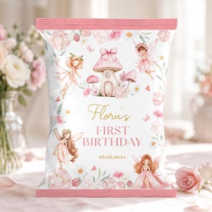 May include: A white snack bag with pink trim featuring illustrations of fairies, mushrooms, and flowers. The text reads Flora's FIRST BIRTHDAY 28.08.202x in gold and pink lettering. The design includes small butterflies and soft floral accents.