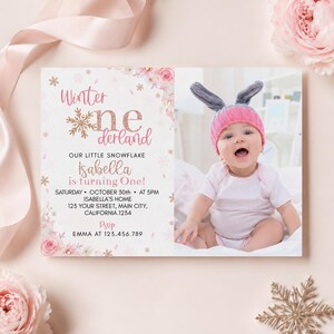 May include: A rectangular birthday invitation card featuring pink floral accents, gold snowflake graphics, and the text Winter onederland. The card includes details for Isabella turning one, with a photo of a baby wearing a pink knit hat with ears.