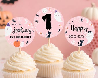 Op de afbeelding: Drie cupcakes met ronde roze papieren toppers met Halloween-motieven. De toppers tonen de tekst Sophia's 1ST BOO.DAY, het cijfer 1 en Happy BOO-DAY! samen met illustraties van spoken, zwarte katten, pompoenen en vleermuizen.