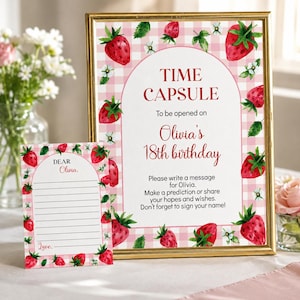 May include: A gold-framed sign and a matching card featuring a pink gingham background with watercolor strawberries and white flowers. The sign reads: TIME CAPSULE To be opened on Olivia's 18th birthday. Please write a message for Olivia.