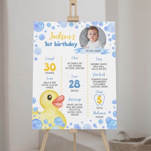 Puede incluir: Un cartel de hitos de primer cumpleaños azul y amarillo con una foto de un bebé. El cartel presenta un pato de goma, burbujas y detalles sobre el peso, la altura, los alimentos favoritos y las primeras palabras del bebé. El texto del cartel dice "Jackson's 1st birthday 10.08.202X".