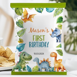 Op de afbeelding: Een witte chipzak met een groene rand en een dinosaurus-thema. De zak heeft de tekst "Mason's First Birthday" met de datum "15.03.202X". De zak heeft een groene, blauwe en oranje dinosaurus-illustratie met groene bladeren.
