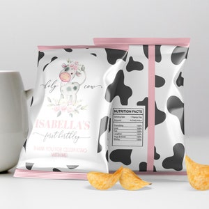 May include: A white and black cow-print chip bag with a pink border. The front of the bag features a watercolor illustration of a cow with pink flowers and the text "Holy Cow Isabella's First Birthday Thank You for Celebrating with Me". The back of the bag has a nutrition facts label.