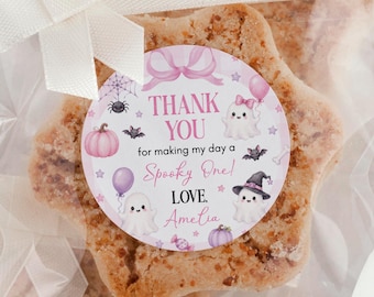 May include: A star-shaped cookie in a clear plastic bag tied with a white ribbon. A round sticker features pink text reading THANK YOU for making my day a Spooky One! LOVE. Amelia, with illustrations of ghosts, a pumpkin, a spider web, and bats.