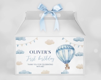May include: White favor box with a blue and white hot air balloon and a teddy bear. The box has a blue ribbon and says "Oliver's First Birthday" and "Thank you for celebrating with me!"  GooberStudioPrints.