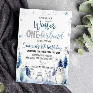 May include: A rectangular invitation card with a white background featuring blue snowflakes and the text "JOIN US IN A Winter ONEderland TO CELEBRATE Cameron's 1st birthday". It includes illustrations of a polar bear, penguins, and a seal.