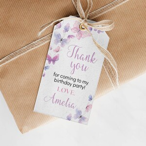 May include: A rectangular white gift tag with a gold eyelet and a natural jute twine bow. The tag features watercolor-style purple and pink butterflies and the text: Thank you for coming to my birthday party! LOVE, Amelia.