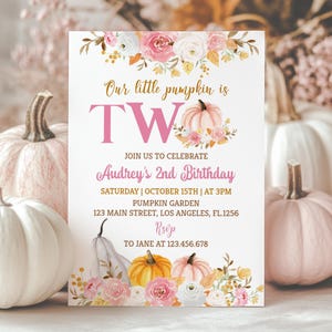 May include: A white invitation card with the text "Our little pumpkin is TWO" in pink and gold. The card is decorated with floral and pumpkin illustrations. The invitation is for Audrey's 2nd birthday, with the date, time, and location.