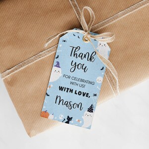 Pu&ograve; includere: Un'etichetta regalo rettangolare azzurra con un occhiello dorato e un fiocco in spago naturale. L'etichetta presenta illustrazioni a tema Halloween con fantasmi, zucche, un gatto nero e ragni, con il testo Thank you FOR CELEBRATING WITH US! WITH LOVE, MASON.