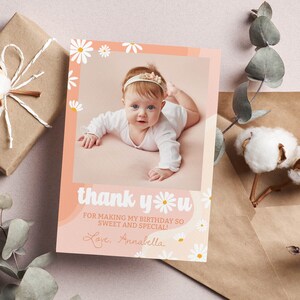 May include: A rectangular thank you card featuring a photo of a baby in a white long-sleeve shirt and headband. The card has a peach background with white daisy illustrations and the text: thank you FOR MAKING MY BIRTHDAY SO SWEET AND SPECIAL! Love, Annabella.