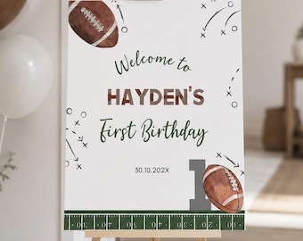 May include: A white rectangular birthday sign on a wooden easel featuring football graphics, the text "Welcome to HAYDEN'S First Birthday", the date "30.10.202X", a large grey number one, and a green football field yard line border at the bottom.