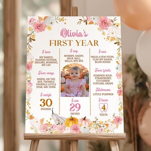 May include: A rectangular milestone sign featuring a floral border with pink and white roses, pumpkins, and text detailing a child's first year. The center displays a photograph of a child, with sections for I love, I say, I can, favorite songs, foods, nickname, weight of 30 pounds, height of 29 inches, and 4 teeth.