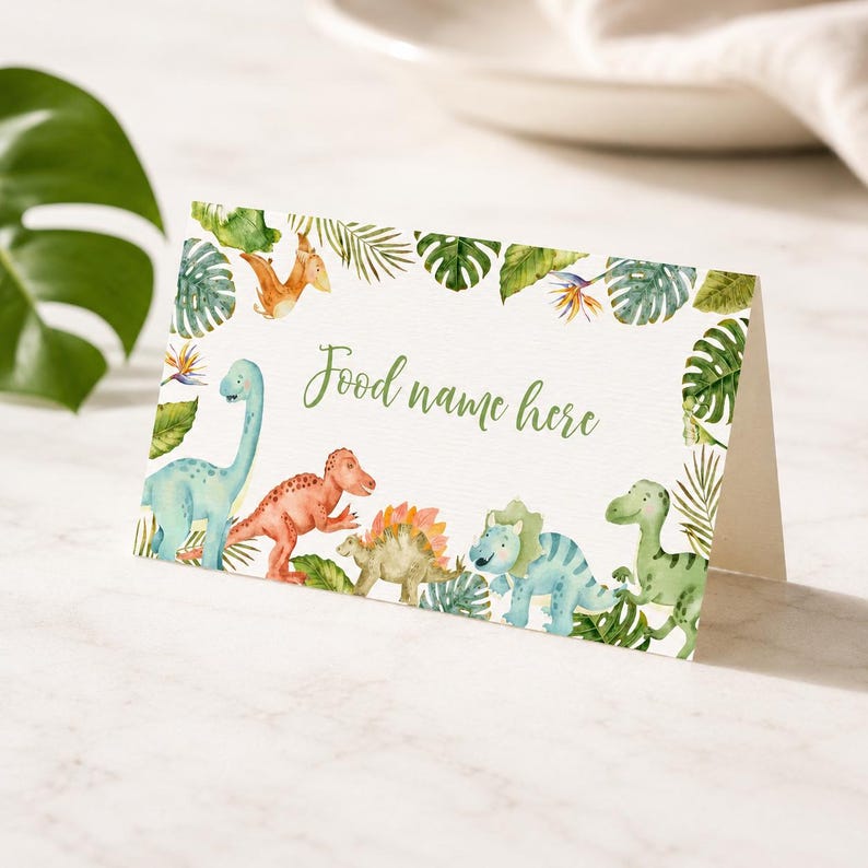 Może przedstawiać: Złożona biała kartka z akwarelową ilustracją r&oacute;żnych dinozaur&oacute;w i tropikalnych liści. Tekst "Food name here" jest nadrukowany zieloną kursywą na środku. Dinozaury obejmują niebieskie, pomarańczowe i zielone gatunki.