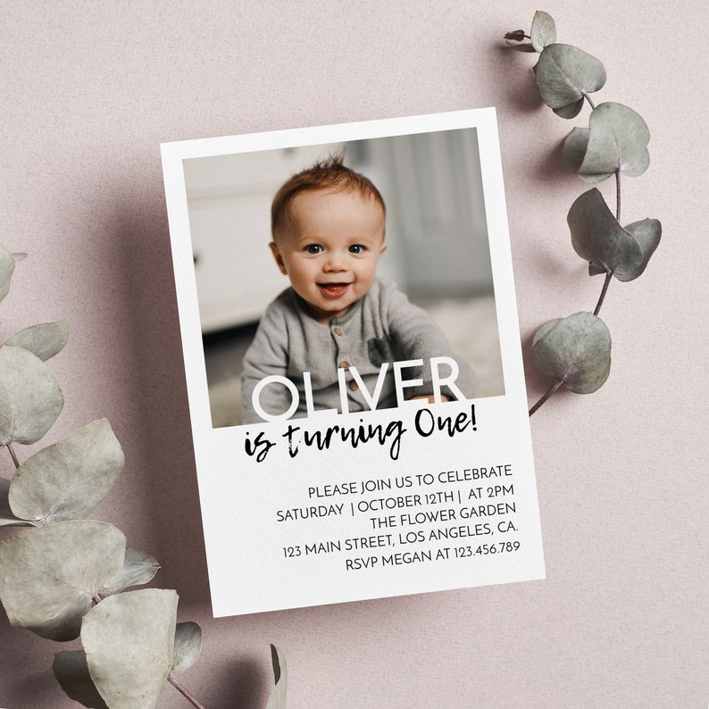 Op de afbeelding: Een rechthoekige verjaardagsuitnodigingskaart met een foto van een lachende baby. De tekst luidt OLIVER is turning One! PLEASE JOIN US TO CELEBRATE SATURDAY | OCTOBER 12TH | AT 2PM THE FLOWER GARDEN 123 MAIN STREET, LOS ANGELES, CA. RSVP MEGAN AT 123.456.789