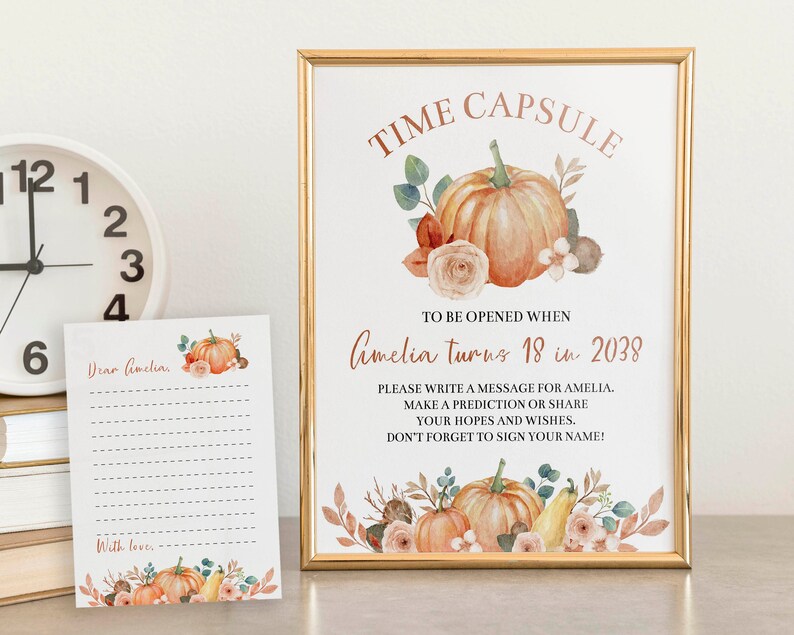 Może przedstawiać: Złota ramka ze znakiem oraz pasująca karta z akwarelowymi dyniami, kwiatami i liśćmi. Znak zawiera napis TIME CAPSULE TO BE OPENED WHEN Amelia turns 18 in 2038 oraz instrukcje dotyczące napisania wiadomości, przewidywań lub życzeń dla Amelii.