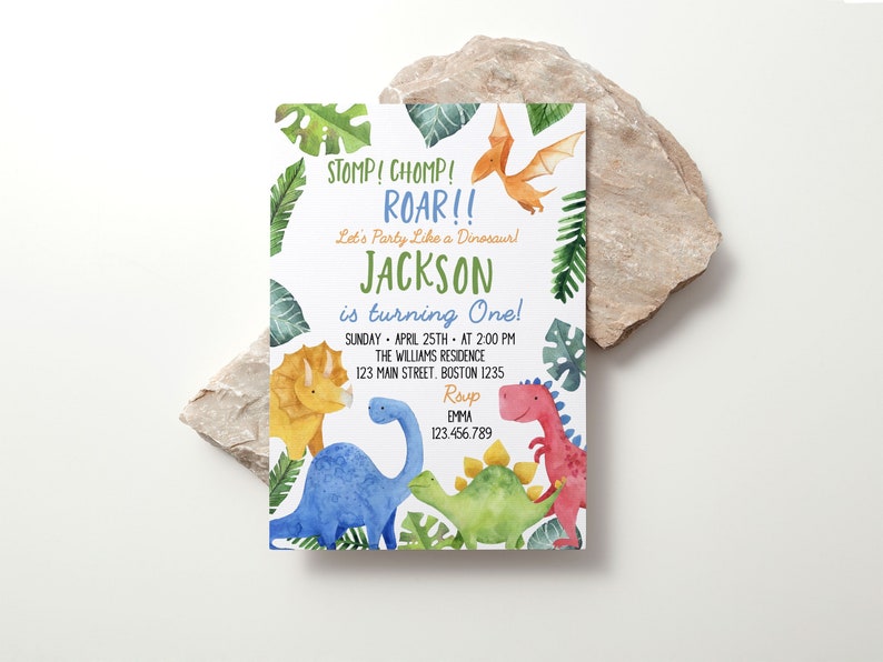 May include: A rectangular birthday invitation card featuring watercolor illustrations of a yellow triceratops, blue long-necked dinosaur, green stegosaurus, red T-Rex, and orange pterodactyl surrounded by green tropical leaves and text.