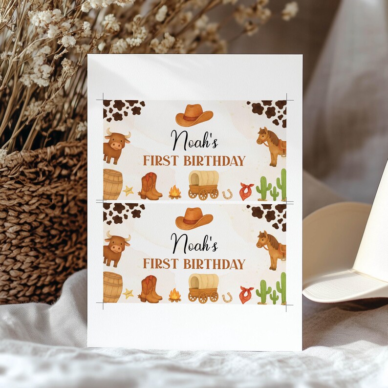 Puede incluir: Una tarjeta rectangular blanca con dos impresiones id&eacute;nticas para el primer cumplea&ntilde;os de Noah. El dise&ntilde;o incluye patrones de piel de vaca marr&oacute;n, un sombrero de vaquero, un toro, un barril, una bota, una fogata, una carreta, una herradura, un pa&ntilde;uelo y un cactus.