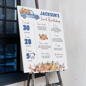 May include: A white rectangular milestone birthday sign featuring a blue truck, orange pumpkins, and text including Jackson's First Birthday, weight of 30 pounds, height of 28 inches, 5 teeth, favorite foods, songs, toys, and personal milestones.
