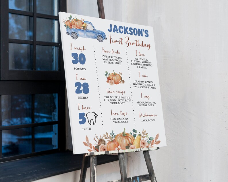 May include: A white rectangular milestone birthday sign featuring a blue truck, orange pumpkins, and text including Jackson's First Birthday, weight of 30 pounds, height of 28 inches, 5 teeth, favorite foods, songs, toys, and personal milestones.