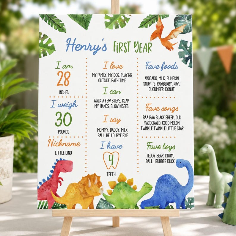 May include: A white milestone board titled Henry's First Year featuring watercolor dinosaur illustrations and tropical leaves. It lists stats including 28 inches, 30 pounds, 4 teeth, favorite foods, songs, and toys in colorful text.