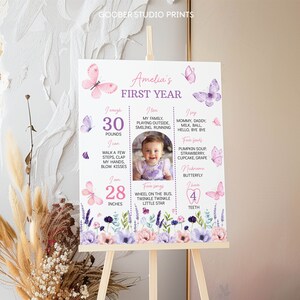 Puede incluir: Un p&oacute;ster imprimible blanco con un dise&ntilde;o floral rosa y morado. El p&oacute;ster est&aacute; decorado con mariposas y presenta una foto de una ni&ntilde;a peque&ntilde;a. El p&oacute;ster incluye el texto "Amelia's First Year" y enumera los hitos de la beb&eacute;, incluyendo el peso, la altura, los alimentos favoritos y las primeras palabras.