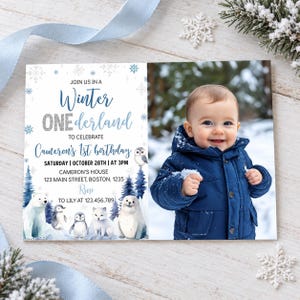 May include: A rectangular birthday invitation card featuring a photo of a child in a navy blue winter jacket on the right. The left side has blue text reading Winter ONEderland, Cameron's 1st birthday, and details, with illustrations of a polar bear, penguins, and a seal.