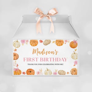 May include: A white gable gift box with a light pink satin ribbon bow on top. The front features a border of watercolor pumpkins, pink roses, and autumn leaves, with the text "Madison's FIRST BIRTHDAY THANK YOU FOR CELEBRATING WITH ME!"