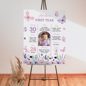 Puede incluir: Un cartel de hitos del primer cumplea&ntilde;os de color rosa y morado con una foto de una ni&ntilde;a. El cartel presenta mariposas, flores y el texto "Amelia's First Year". Tambi&eacute;n incluye detalles sobre el peso, la altura, los alimentos favoritos, las canciones y las palabras de la ni&ntilde;a.