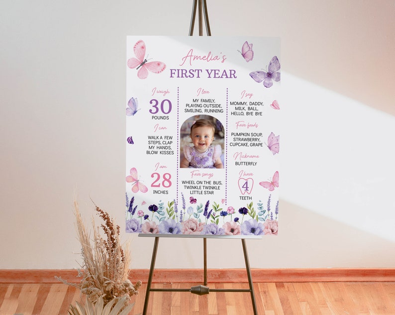 Puede incluir: Un cartel de hitos del primer cumplea&ntilde;os de color rosa y morado con una foto de una ni&ntilde;a. El cartel presenta mariposas, flores y el texto "Amelia's First Year". Tambi&eacute;n incluye detalles sobre el peso, la altura, los alimentos favoritos, las canciones y las palabras de la ni&ntilde;a.
