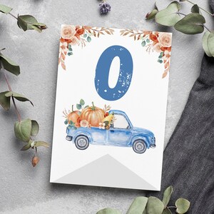 May include: A rectangular white card featuring a large blue number zero at the top centre. Below the number is a blue pickup truck carrying orange pumpkins and autumn foliage. The top corners are decorated with orange roses and brown leaves.