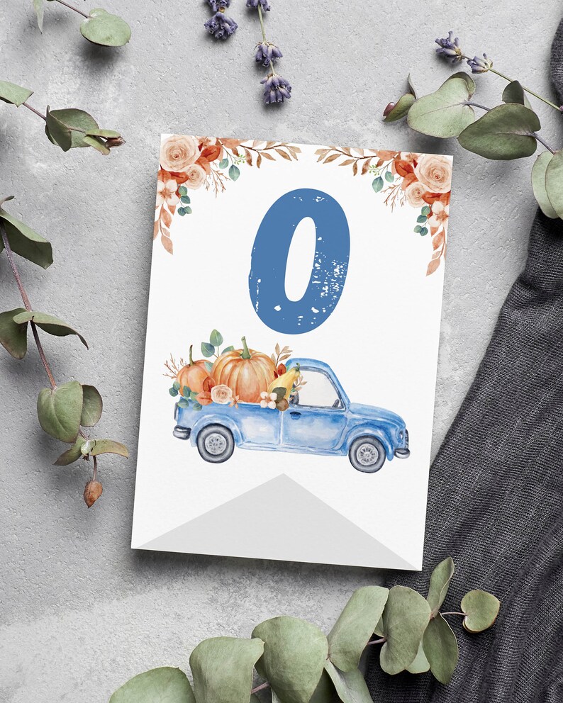 May include: A rectangular white card featuring a large blue number zero at the top centre. Below the number is a blue pickup truck carrying orange pumpkins and autumn foliage. The top corners are decorated with orange roses and brown leaves.