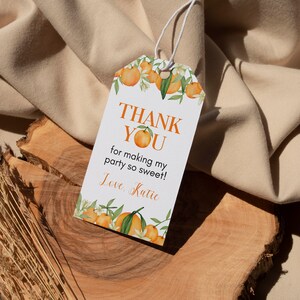 Pu&ograve; includere: Un cartellino regalo rettangolare in carta bianca con un foro e un cordino bianco nella parte superiore. Il cartellino presenta un bordo ad acquerello con arance e foglie verdi e il testo THANK YOU for making my party so sweet! Love, Katie.