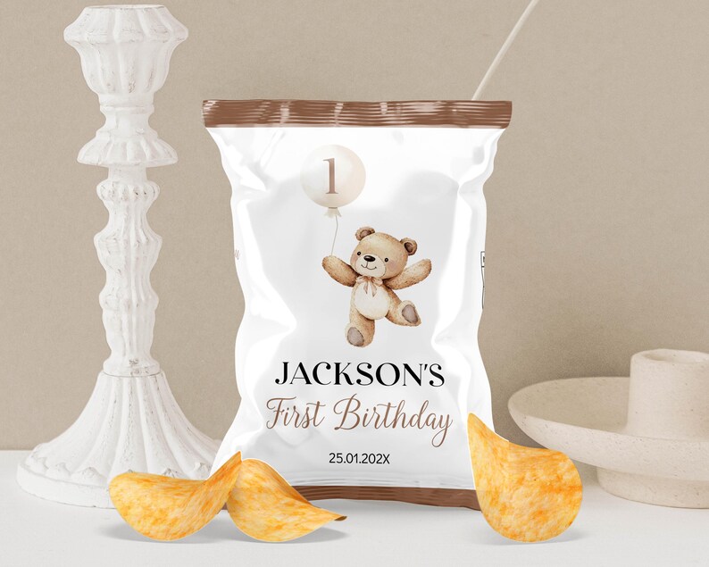 May include: A brown paper bag with a white label that says "JACKSON'S First Birthday" and has a teddy bear with a balloon that says "1" on it. The date "25.01.202X" is printed on the label.