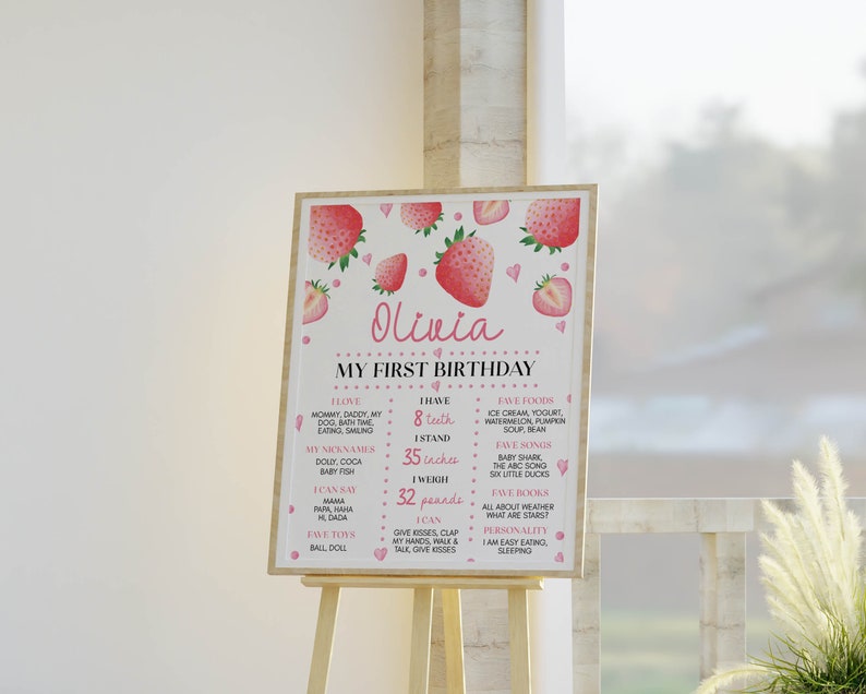 May include: A rectangular birthday milestone sign featuring pink strawberry illustrations and the name Olivia. The text includes My First Birthday, I Love, I Have 8 teeth, I Stand 35 inches, I Weigh 32 pounds, I Can, Fave Foods, Fave Songs, Fave Books, and Personality.