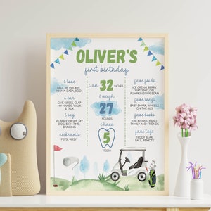May include: A green and blue illustrated first birthday poster for a boy named Oliver. The poster features a golf buggy, a golf ball, and a golf flag. It includes details about Oliver's height, weight, and number of teeth. The poster also lists Oliver's favourite foods, songs, books, and toys.