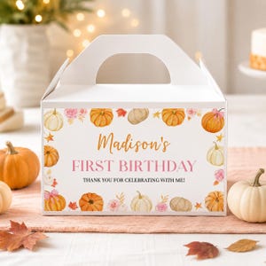 May include: A white cardboard gable box featuring a watercolor print of orange and white pumpkins, pink roses, and autumn leaves. The text reads: Madison's FIRST BIRTHDAY THANK YOU FOR CELEBRATING WITH ME! The box has a handle and a rectangular shape.