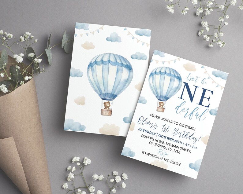 Pu&ograve; includere: Due biglietti d'invito di compleanno rettangolari con un'illustrazione ad acquerello di una mongolfiera blu e bianca che trasporta un orsacchiotto marrone. Il design include nuvole azzurre e beige, festoni e il testo Isnt he ONEderful.