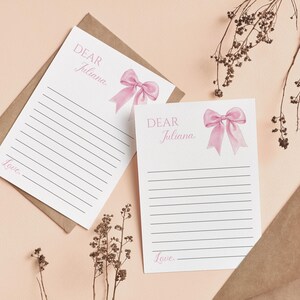 May include: Two blank white cards with pink bows and the text "Dear Juliana" and "Love" on each card. The cards are on a light pink background.