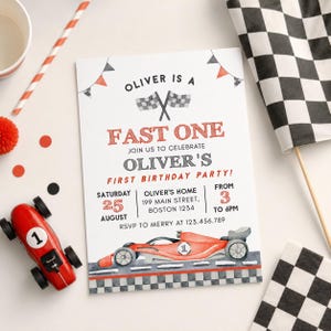 May include: A birthday party invitation with a race car theme. The invitation reads "Oliver is a Fast One" and includes details for the party. A red toy race car and checkered flags are also present.
