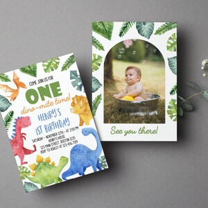 May include: Two rectangular birthday invitation cards featuring watercolor dinosaur illustrations and green tropical leaves. The left card displays text including ONE, dino-mite time!, HENRY'S 1ST BIRTHDAY, and event details. The right card features an arched photo frame with a child in a tub and the text See you there!.