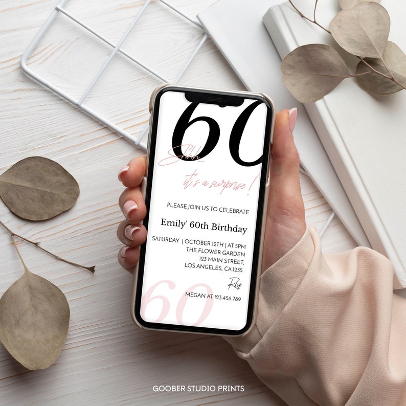 K&ouml;nnte beinhalten: Ein Smartphone mit einer digitalen Einladung zum 60. &Uuml;berraschungsgeburtstag. Auf dem Bildschirm steht in gro&szlig;er schwarzer Schrift 60, Shhh... it's a surprise!, Emily' 60th Birthday sowie Veranstaltungsdetails, Datum, Ort und Kontaktinfos.