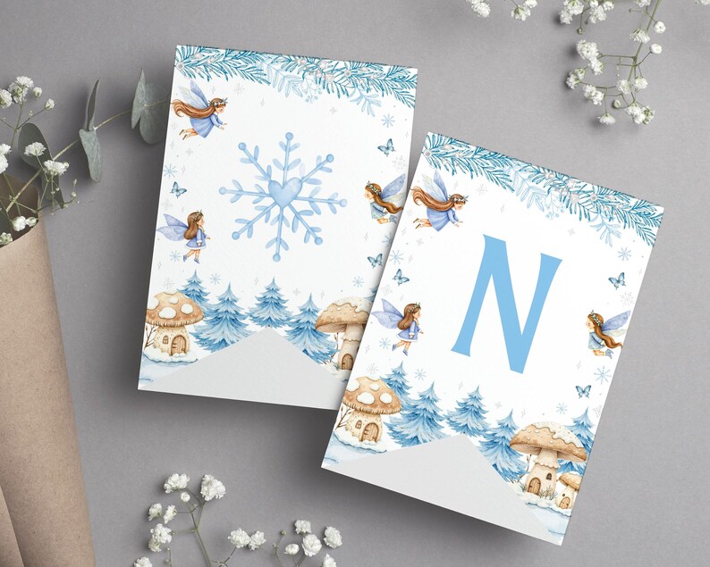 May include: Two white pennant flags featuring a winter theme with blue pine trees, mushroom houses, and flying fairies. One flag displays a large blue snowflake with a heart center, while the other features a large blue letter N in the center.
