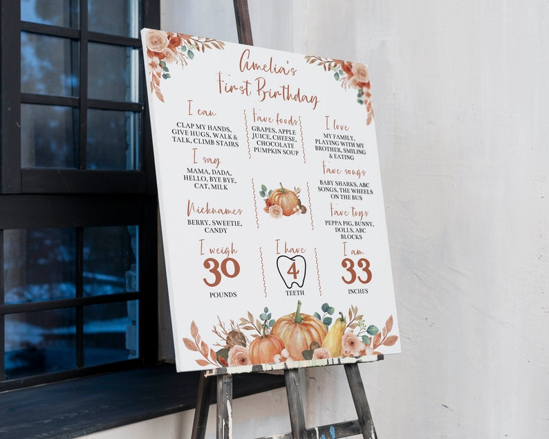 May include: A white milestone birthday sign for Amelia featuring orange pumpkin and floral illustrations. The text lists milestones including 30 pounds, 4 teeth, and 33 inches, alongside favorite foods, songs, and nicknames in a rust-colored font.