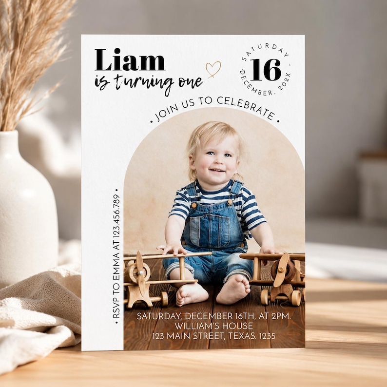 May include: A birthday invitation card featuring a photo of a toddler in denim overalls and a striped shirt sitting with wooden toy airplanes. The text reads Liam is turning one, Saturday December 16, 20XX, Join us to celebrate, and RSVP details.