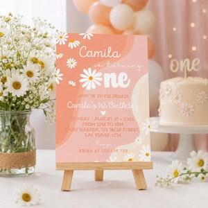 Peut inclure: Une pancarte d'invitation d'anniversaire rectangulaire sur un chevalet en bois avec un fond ondul&eacute; p&ecirc;che et cr&egrave;me et des marguerites blanches. Le texte indique : Camila is turning one, Join us to celebrate Camila's 1st Birthday, Sunday, August 10, 202X.